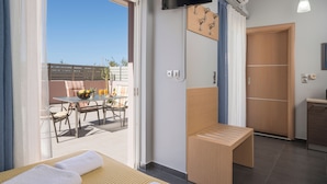 Une chambre d’hôtel moderne dotée d ’un balcon, d’une télévision, d’un banc en bois et d’un coin repas avec une table et des chaises.