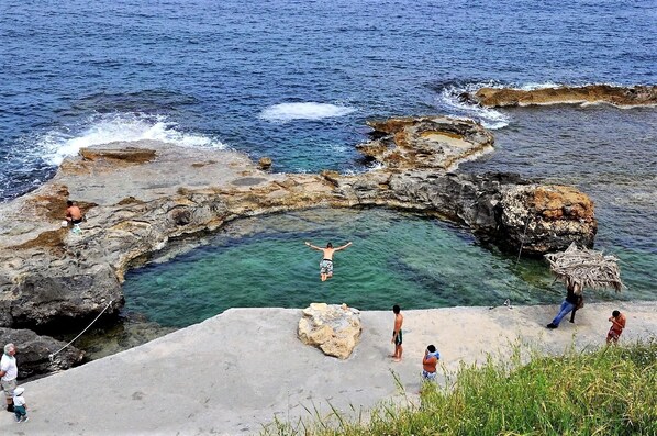 A rocky coastal area with clear water, a person diving, and several people on the shore. - Astrantia-Adults Only (Chania)