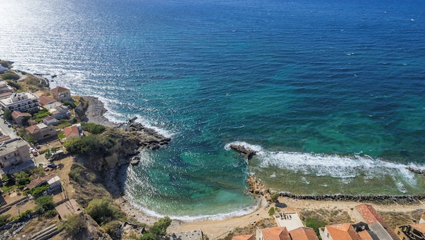 Une ville côtière avec des bâtiments qui bordent la plage, une eau d’un bleu limpide et un promontoire rocheux.