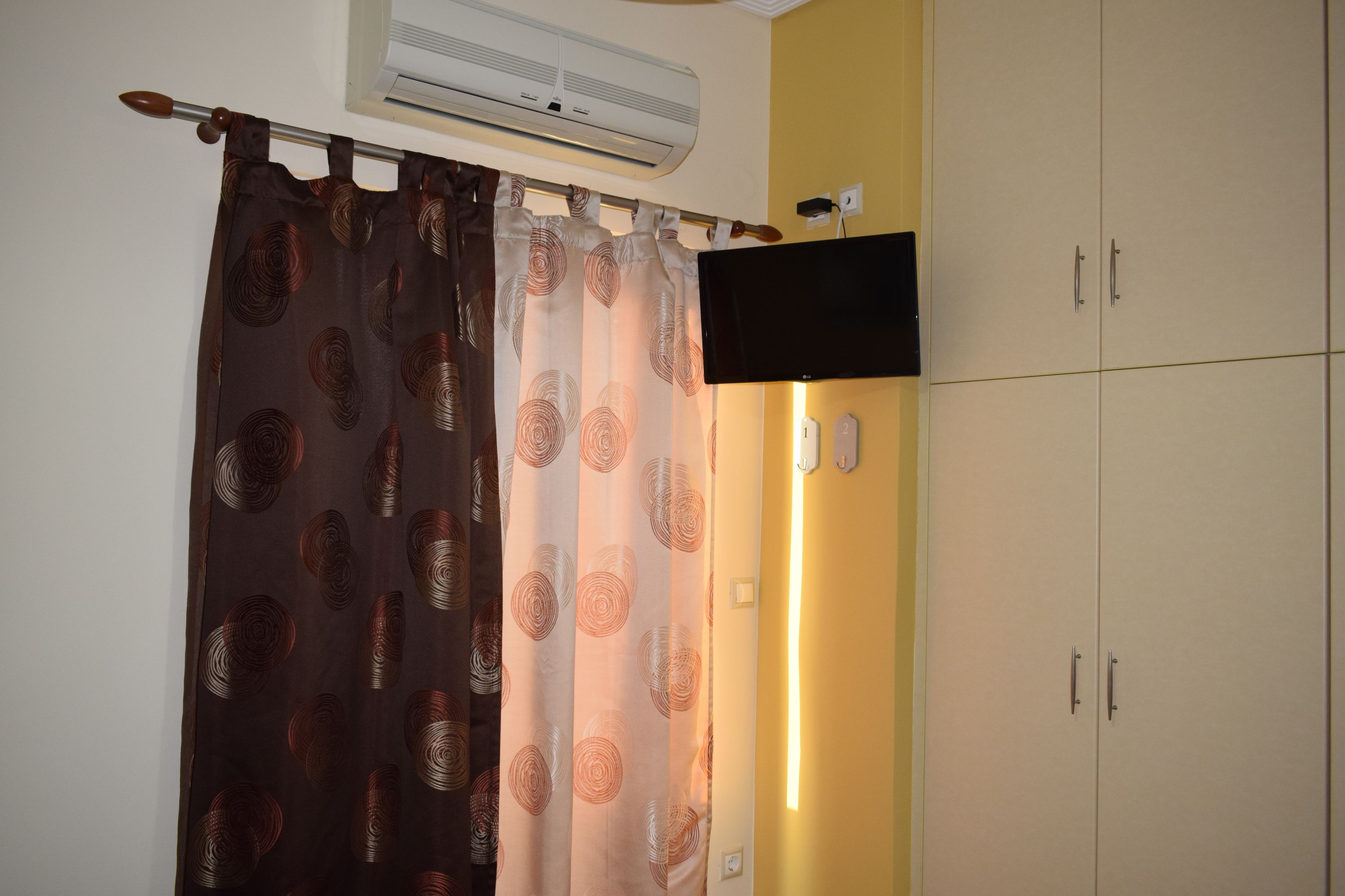 Une pièce avec un rideau, un téléviseur à écran plat fixé au mur et une armoire à deux portes.