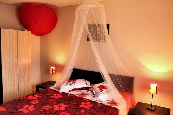 Un lit à baldaquin, une décoration en forme de cœur rouge et deux lampes de chevet.