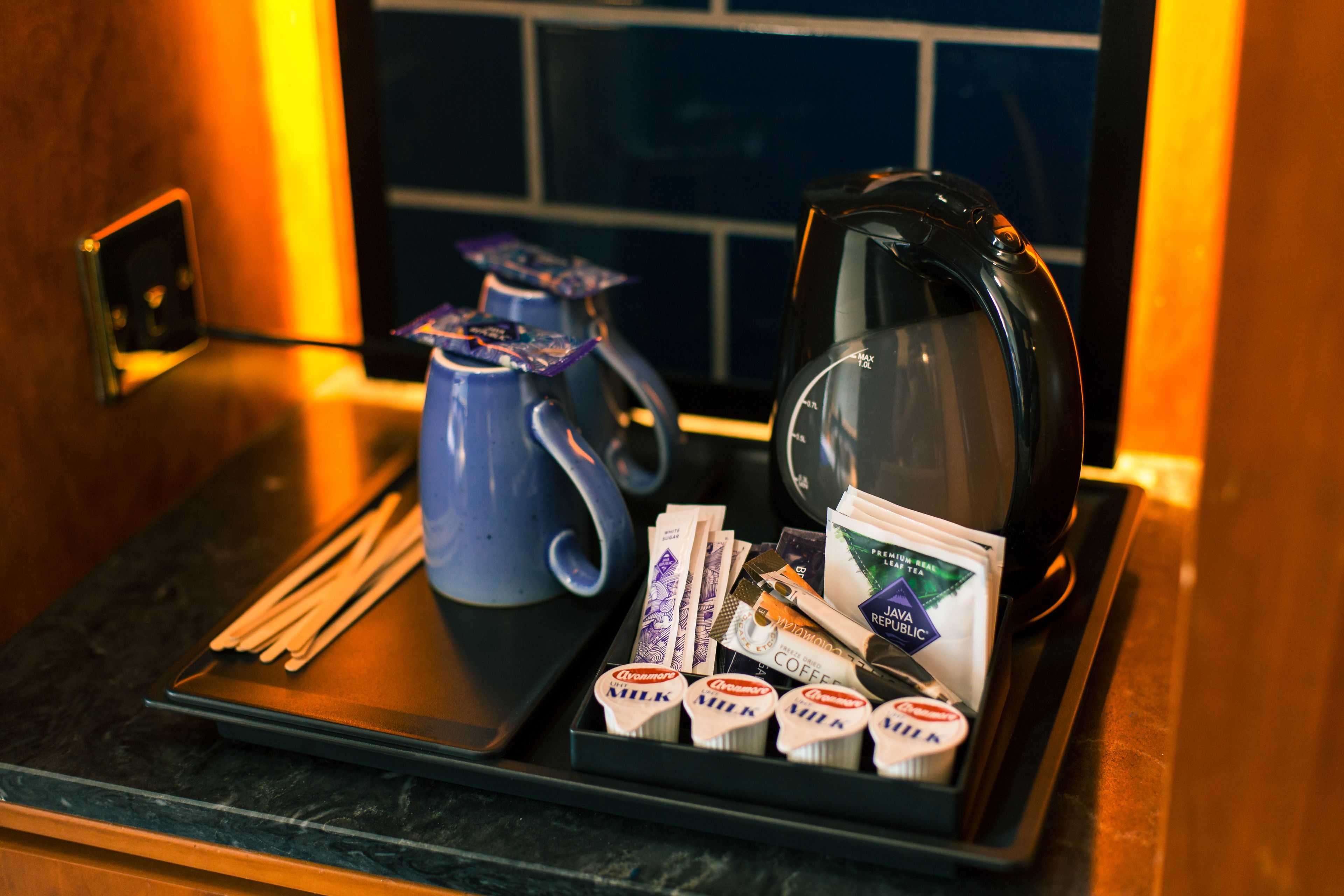 A tray with a blue teapot, a coffee pot, and various coffee packets and milk cartons.