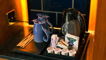 A tray with a blue teapot, a coffee pot, and various coffee packets and milk cartons.