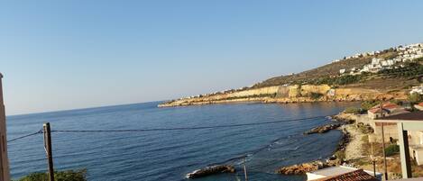 A coastal view with a clear sky, rocky shoreline, and buildings along the coast.
