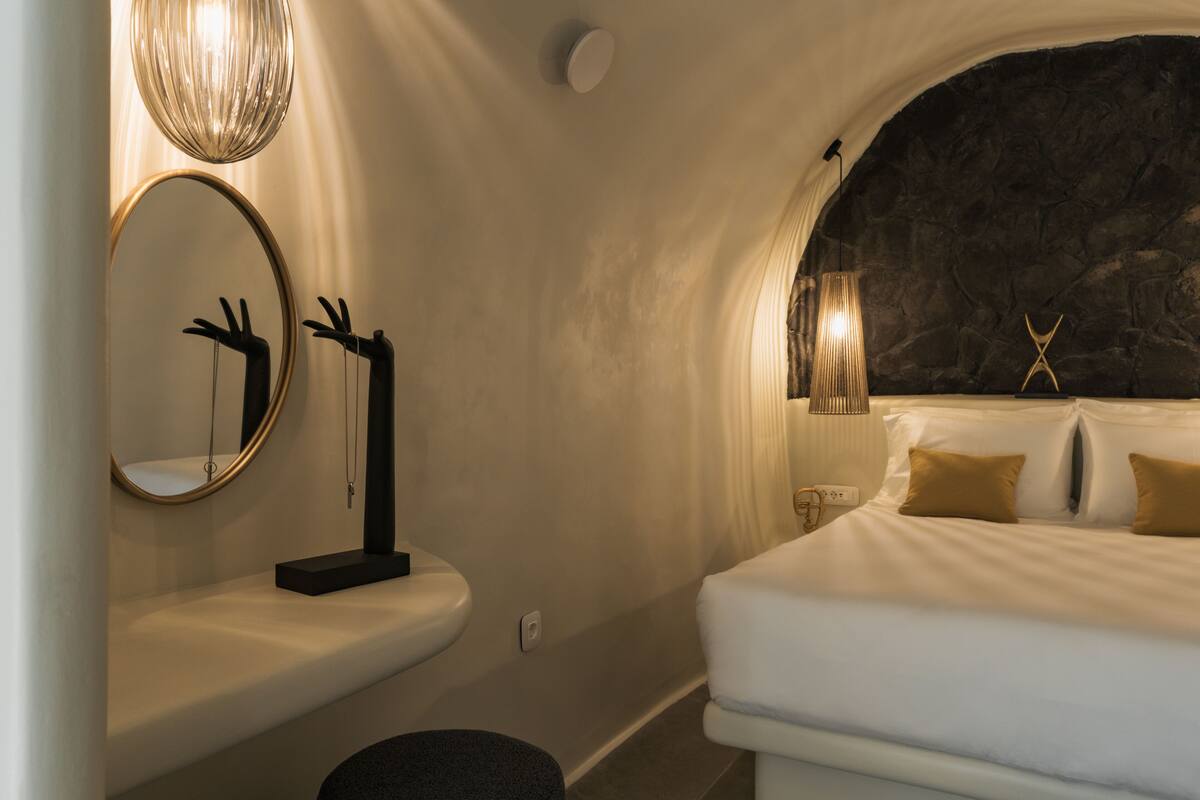 A bedroom with a bed, a round mirror, a small table, and a wall-mounted light fixture.