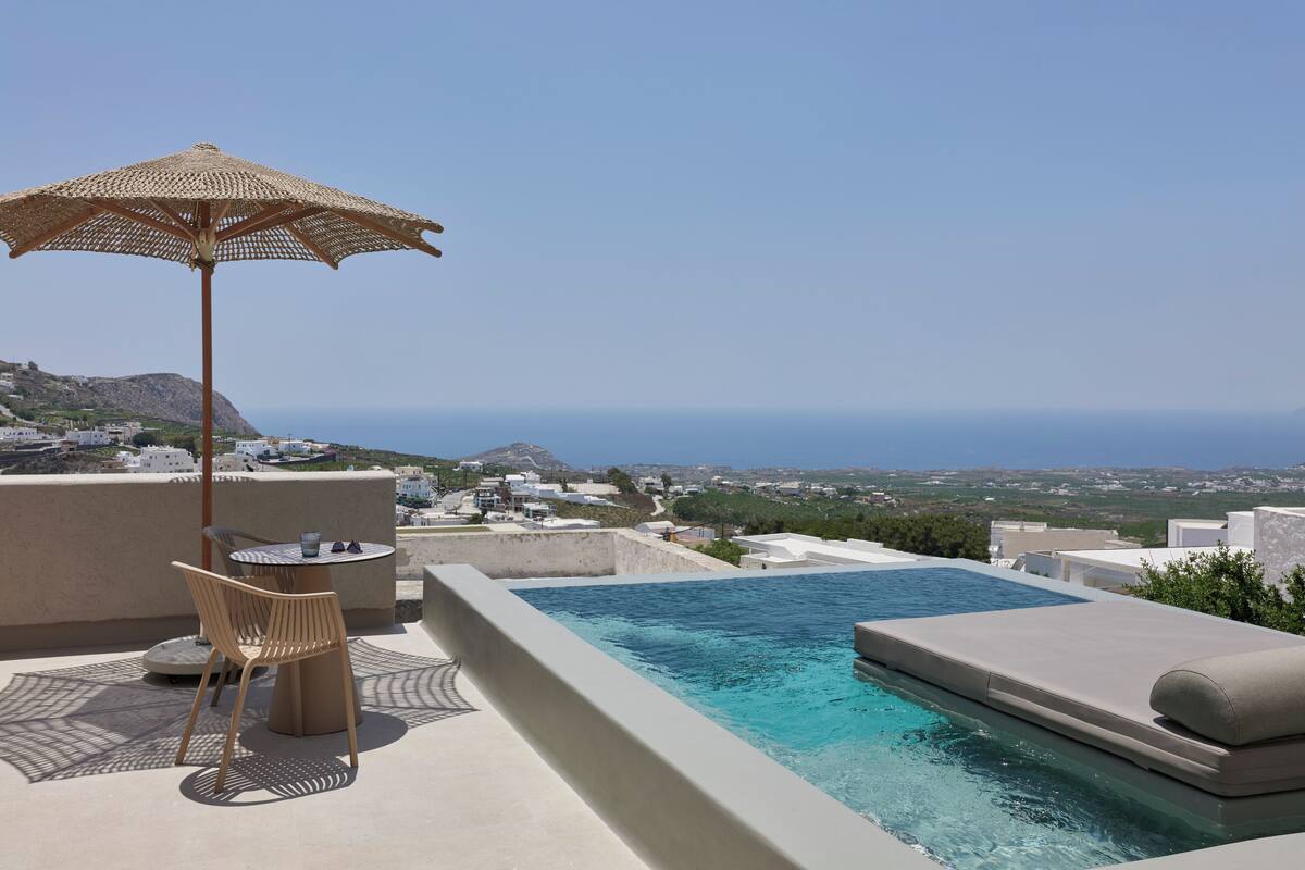 A rooftop infinity pool with a view of the sea, a table with chairs, and a woven umbrella.