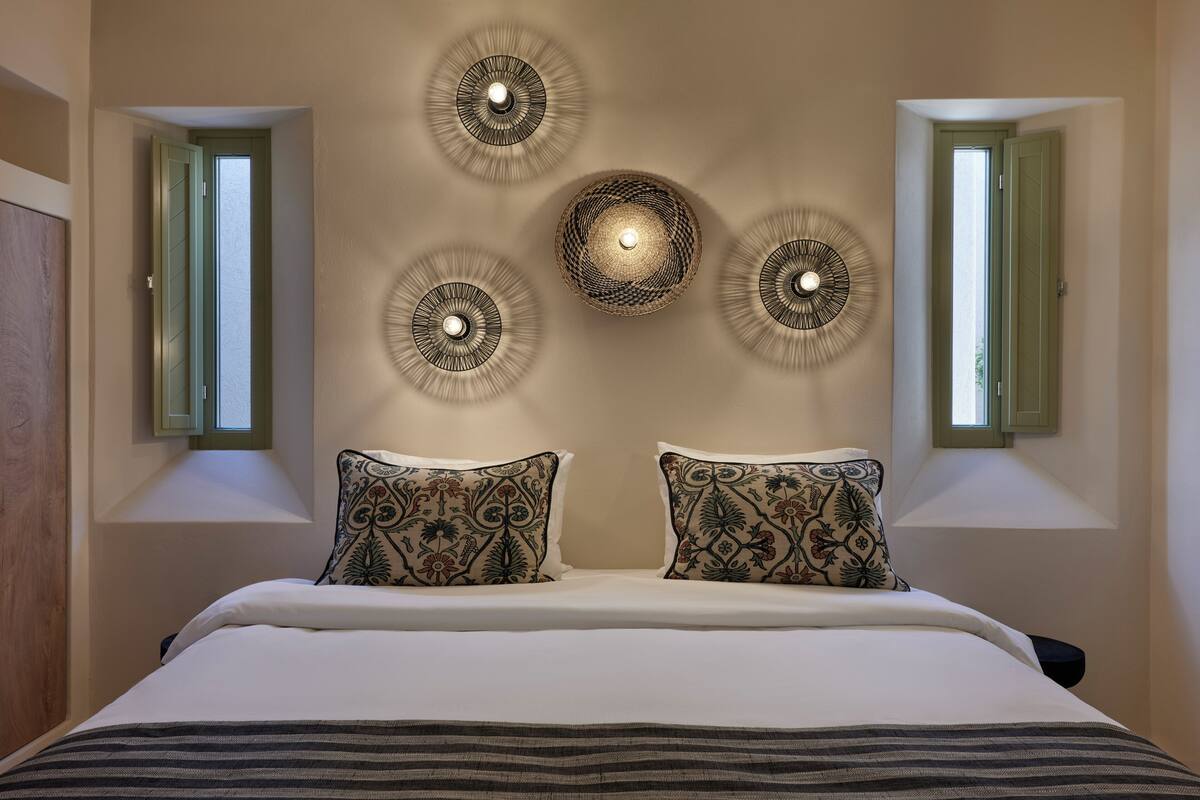 A bedroom with a bed, two decorative wall lights, and two windows with green shutters.