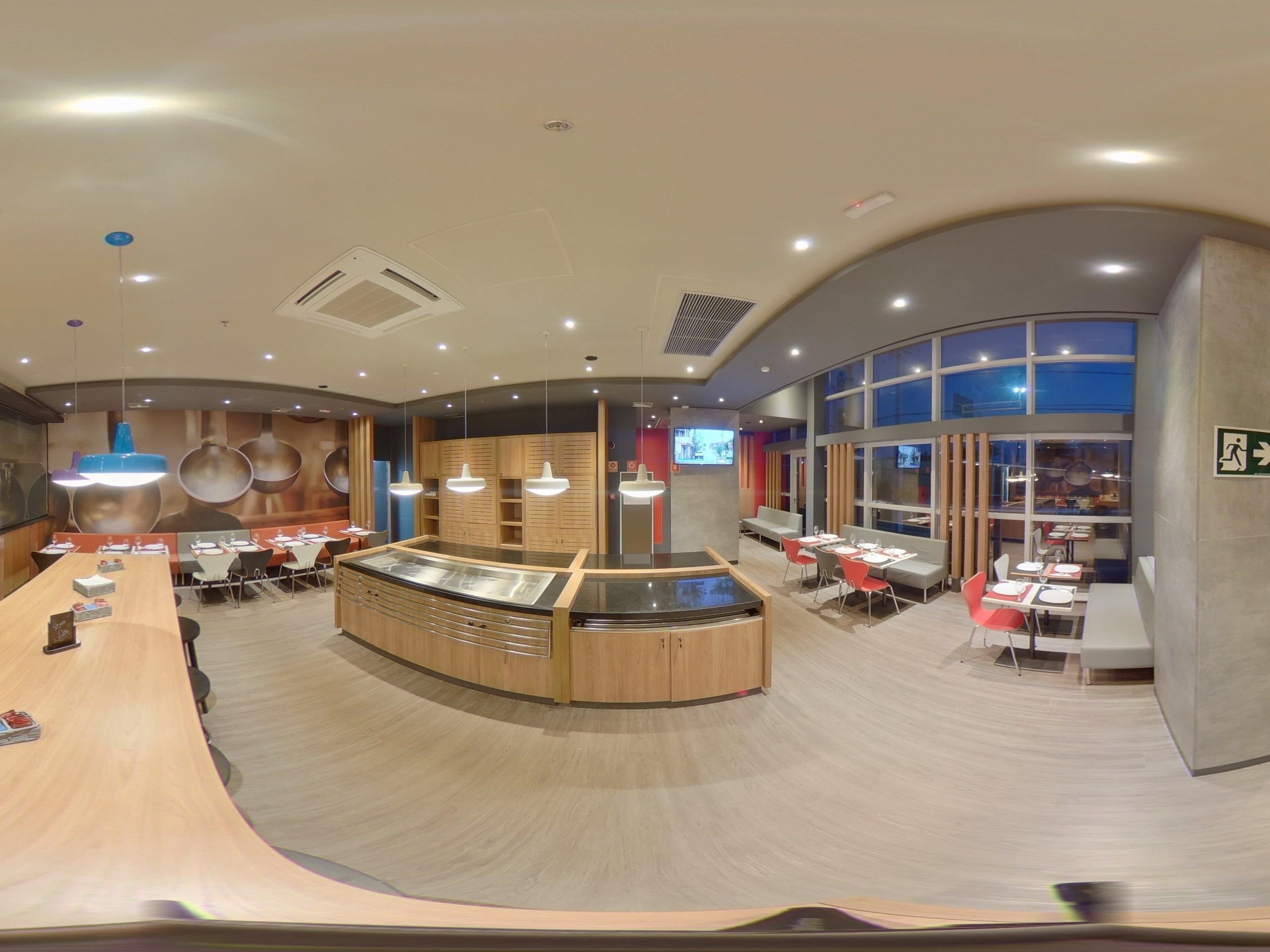 A modern restaurant with a central counter, multiple dining areas, and large windows.