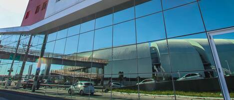A modern building with a glass facade reflecting the sky and nearby structures.