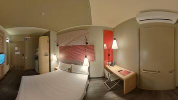 A hotel room with a bed, desk, chair, and an air conditioning unit.