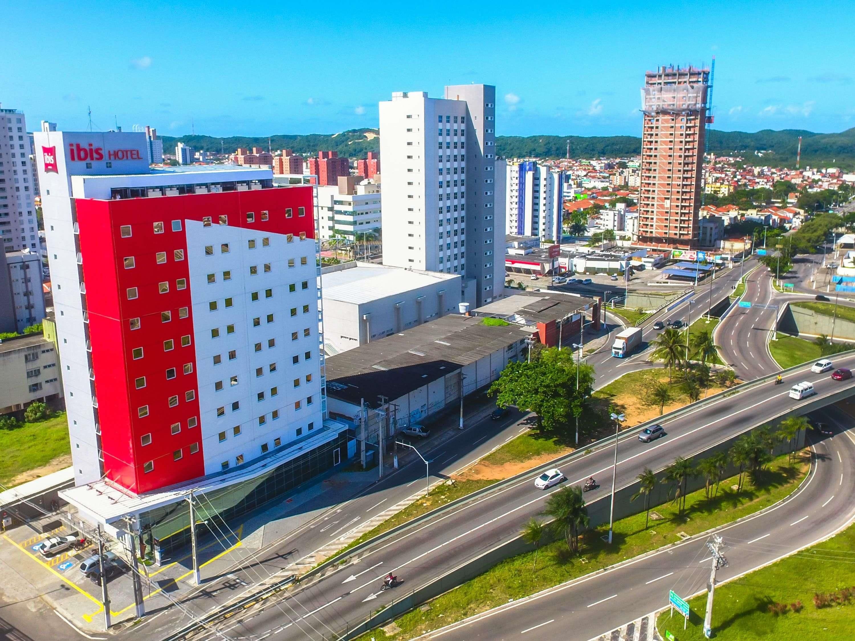 A hotel with a red and white facade, multiple floors, and a parking area.