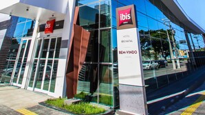 A modern hotel entrance with glass doors, a prominent red and black sign, and a metal sculpture.