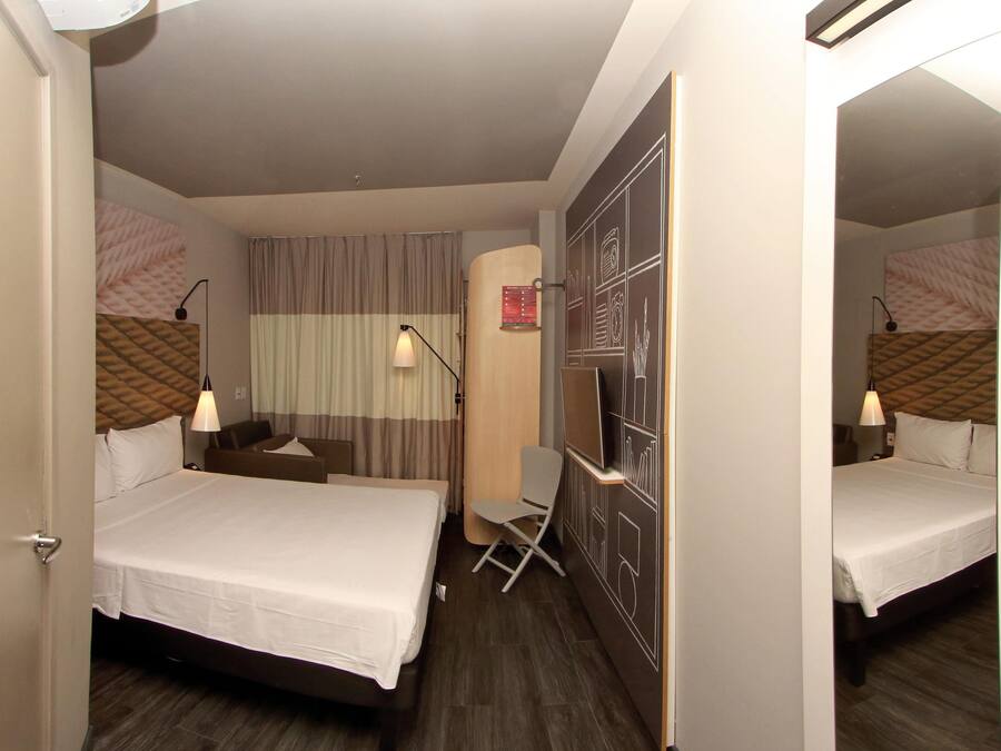 Una habitación de hotel con cama, escritorio, silla, televisor y espejo.
