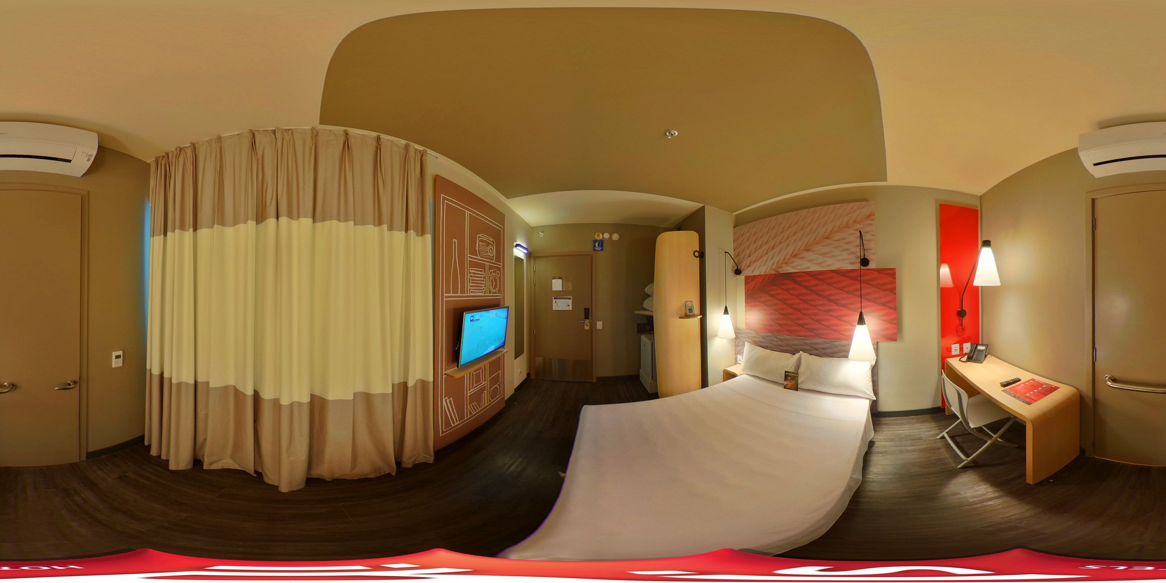 Una habitación de hotel con distribución curvada, televisor, escritorio con silla y cama.
