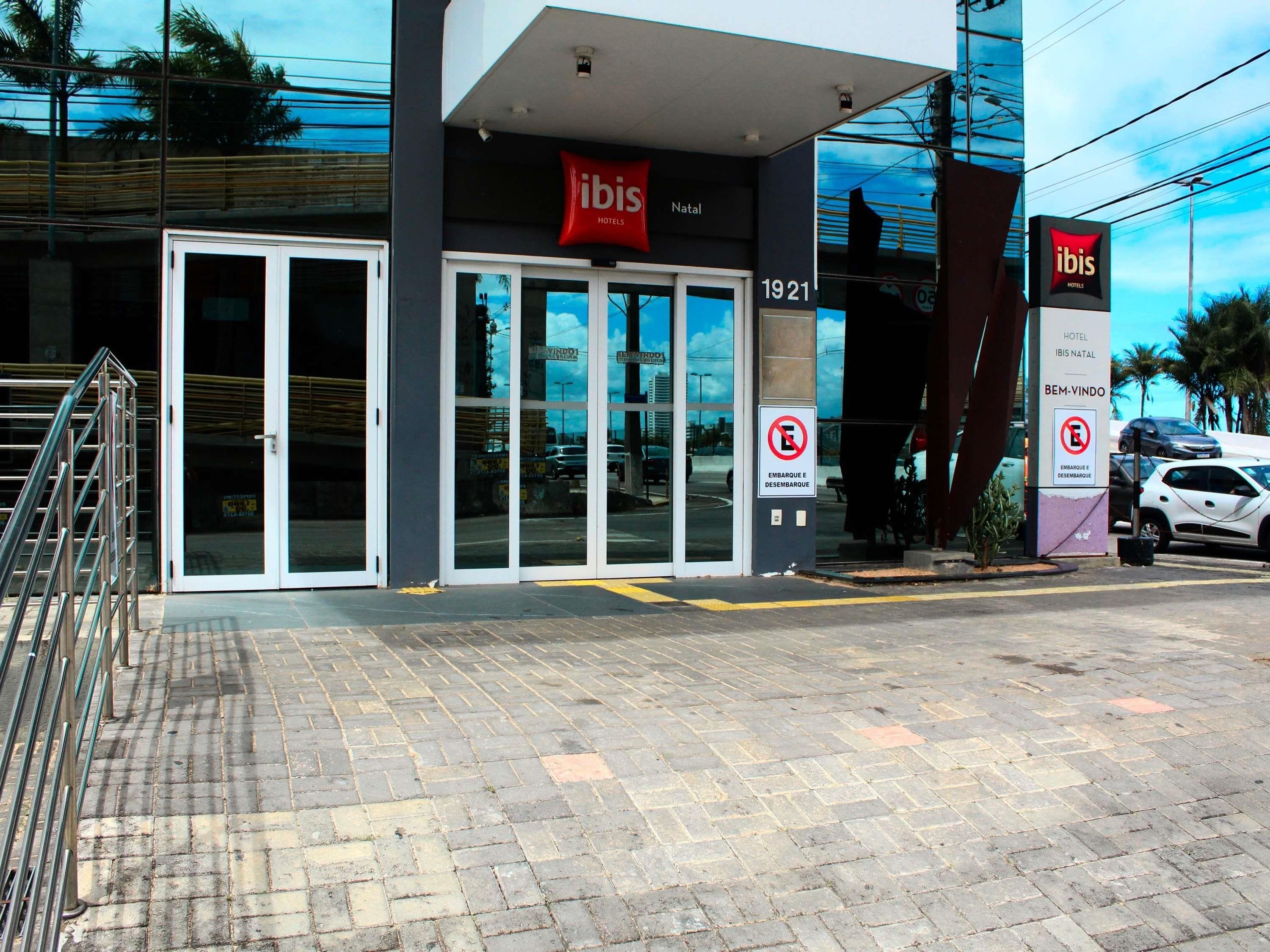 A hotel entrance with glass doors, a sign for ibis hotels, and a no parking sign.