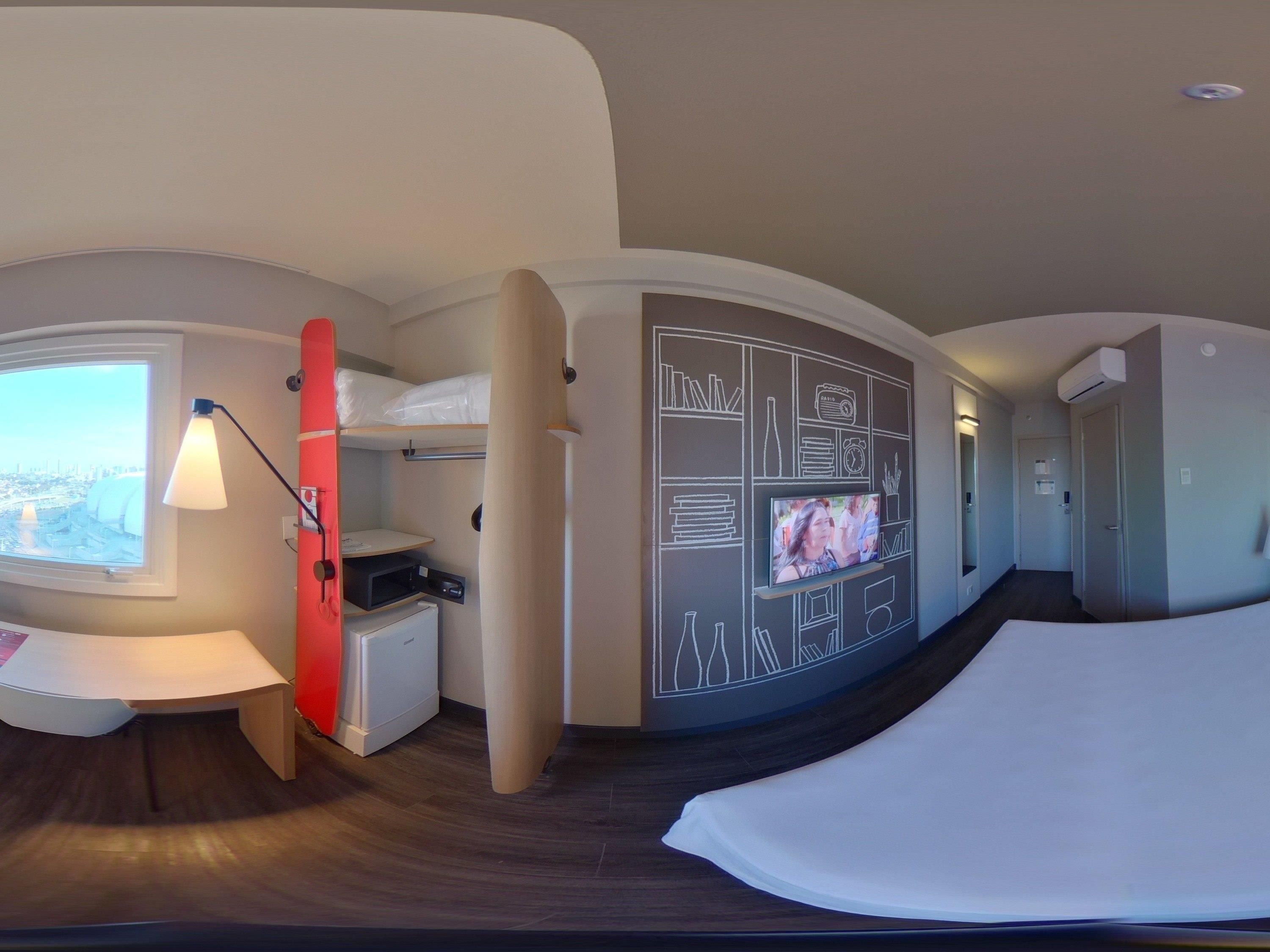 A hotel room with a bed, a TV, a desk, a lamp, and a window with a city view.