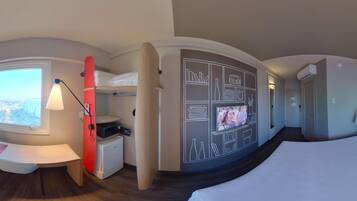 A hotel room with a bed, a TV, a desk, a lamp, and a window with a city view.