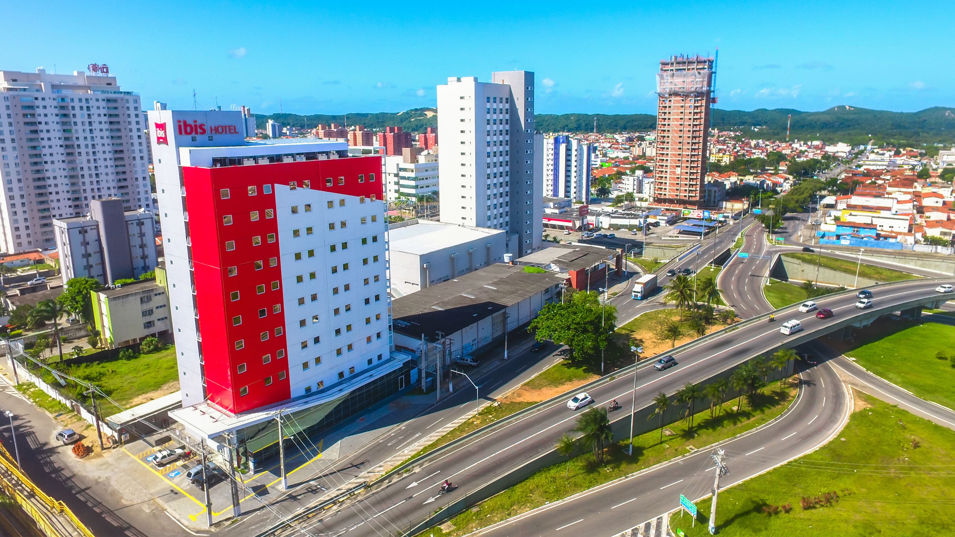 Un hotel moderno con una fachada llamativa de color rojo y blanco, situado cerca de una autopista concurrida con múltiples carriles y puentes.