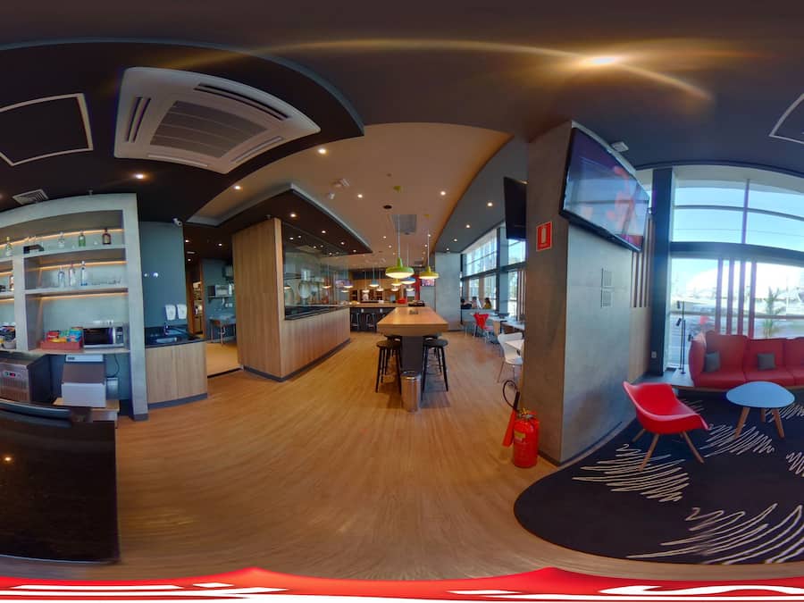 Un interior moderno con una zona de bar curva, asientos con sillas rojas y ventanas amplias que dejan entrar luz natural.