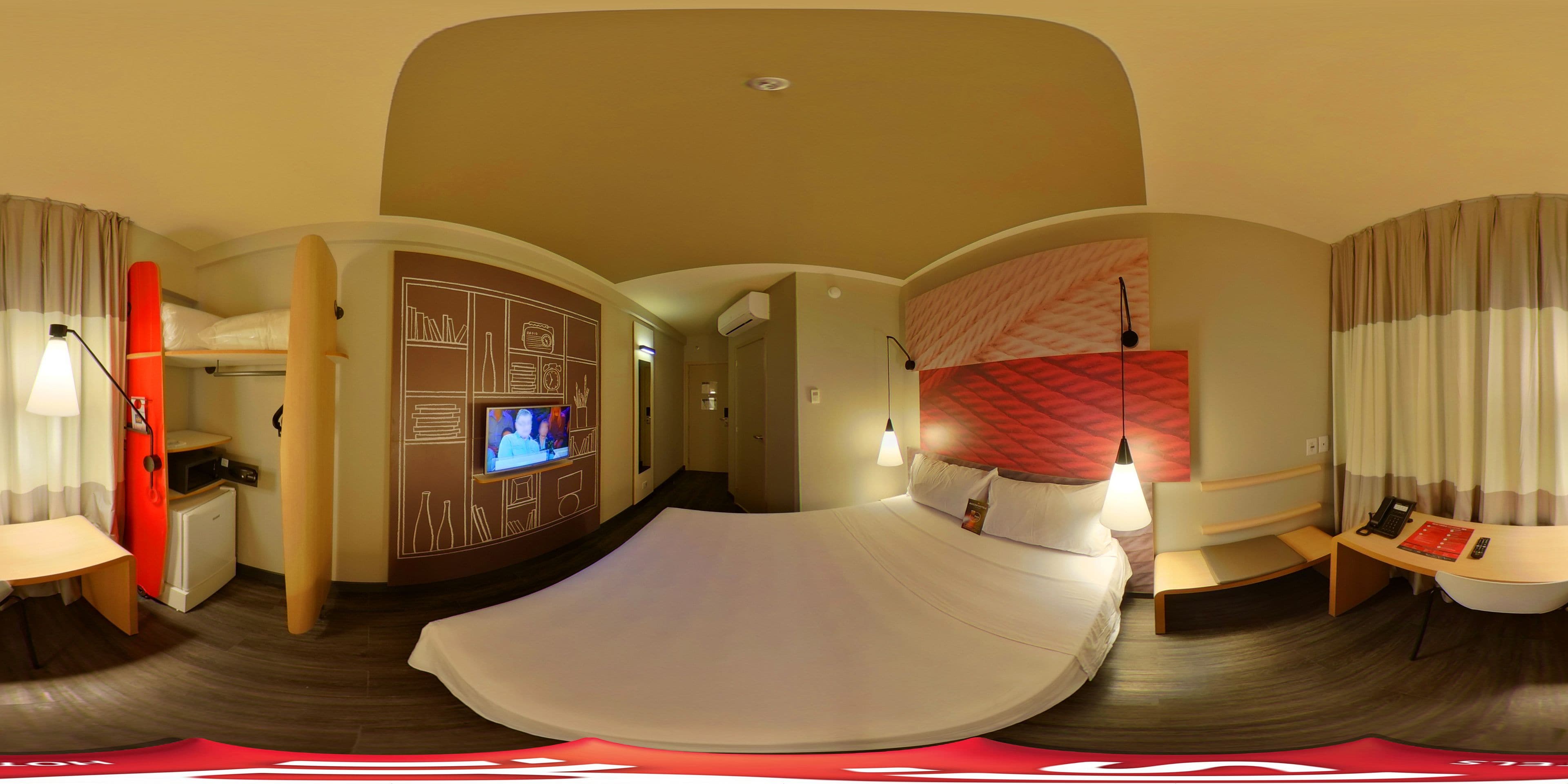 Quarto de hotel com cama, escrivaninha, televisão e banheiro.