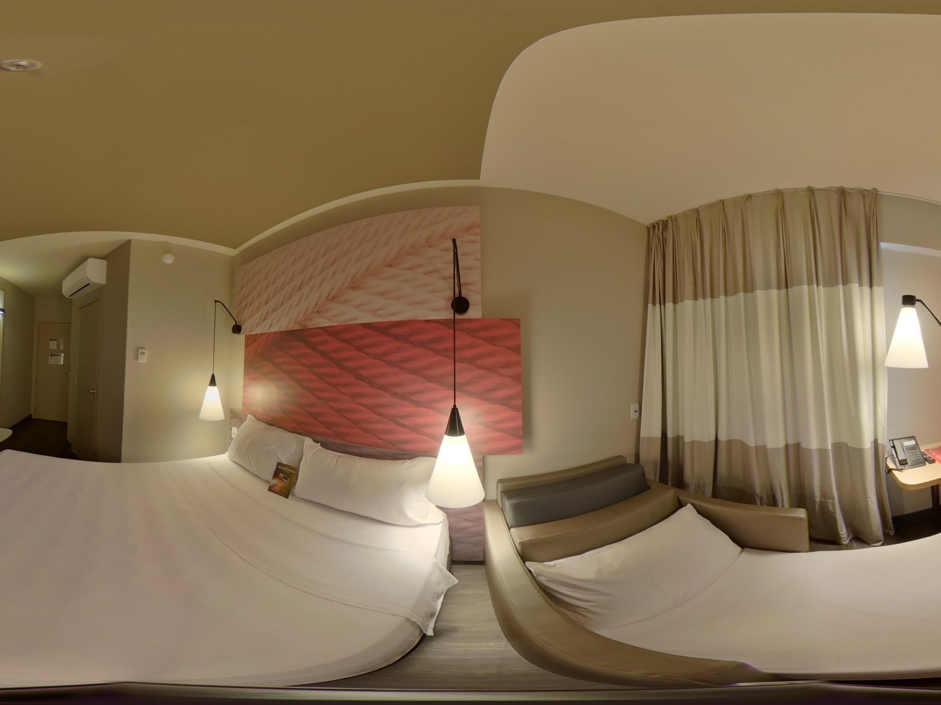 A hotel room with a curved bed, a large wall mural, and a separate seating area with a lamp.