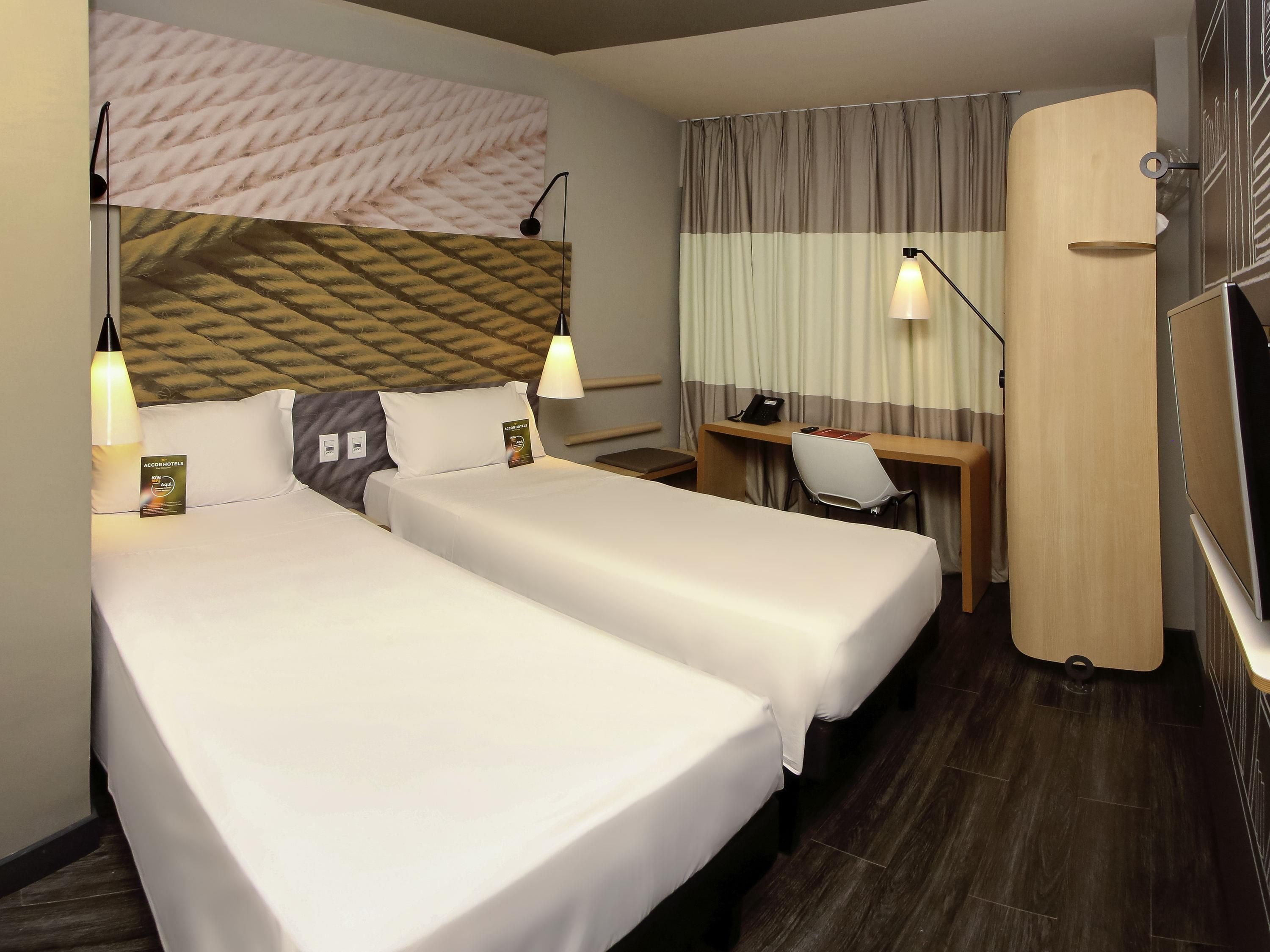 Une chambre d’hôtel avec deux lits, un bureau, une chaise, une lampe et un téléviseur.