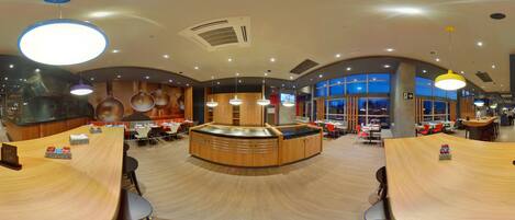 A modern restaurant with a central counter, multiple seating areas, and a large window providing a view of the outside.