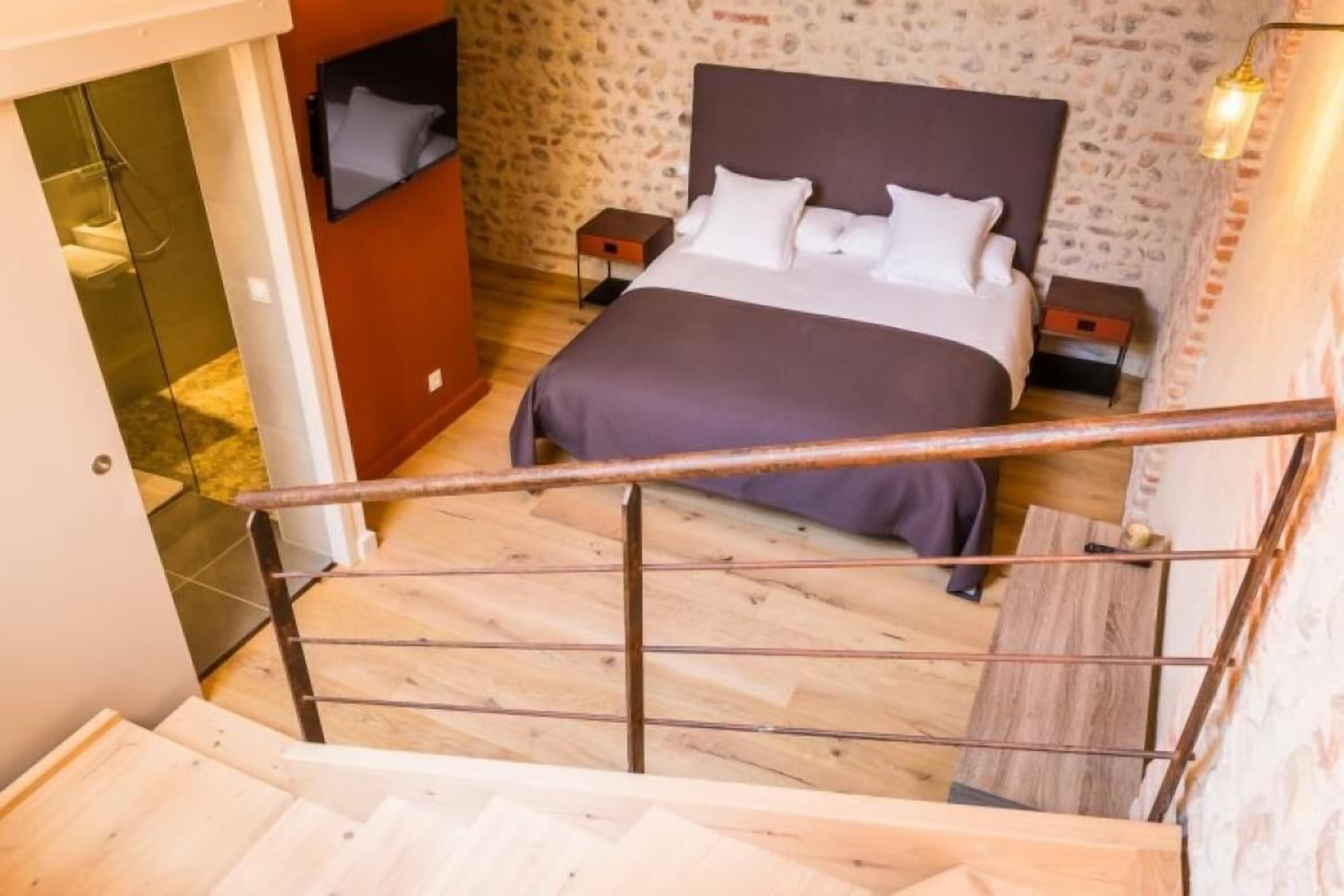 Un dormitorio con cama, mesitas de noche, una escalera de madera y una pared de piedra.