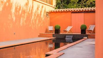 A swimming pool with two lounge chairs and potted plants, surrounded by orange walls and a tiled roof.