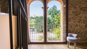 Una habitación con piso de madera, una silla gris y vistas a través de un vano con dos arcos.