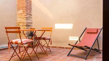 A patio with a table and four chairs, a red lounge chair, and a brick wall.