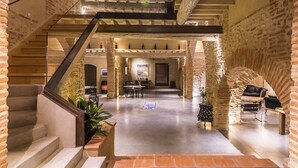 Un interior espacioso con una escalera que conduce a un entresuelo, paredes de piedra y un comedor con mesas y sillas.