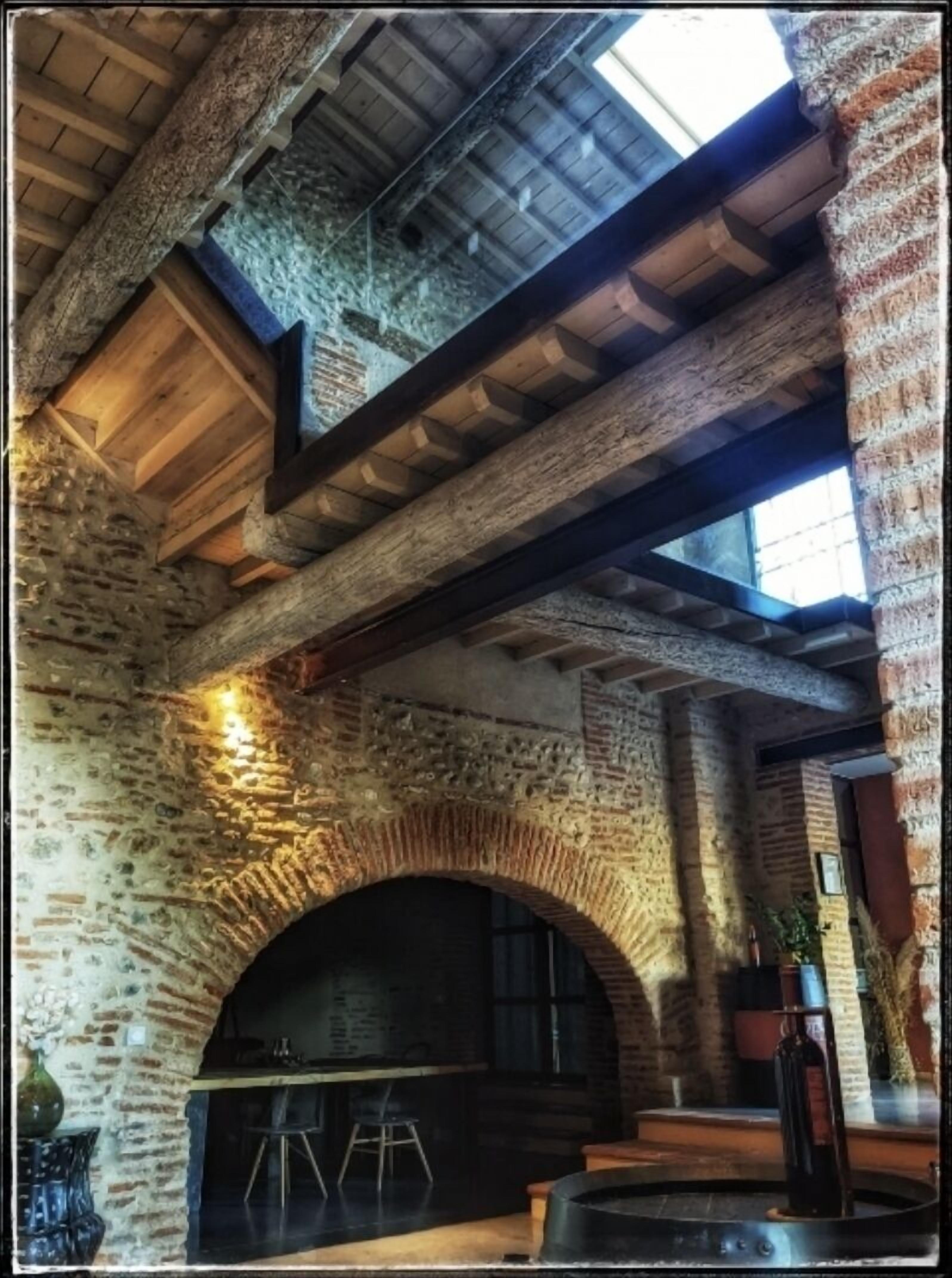 A rustic interior with exposed brick walls, a vaulted ceiling, and a large arched fireplace.