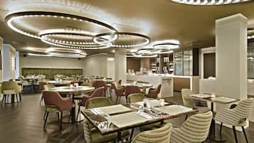 Un restaurante moderno con mesas redondas, sillas tapizadas de verde y lámparas de techo circulares.
