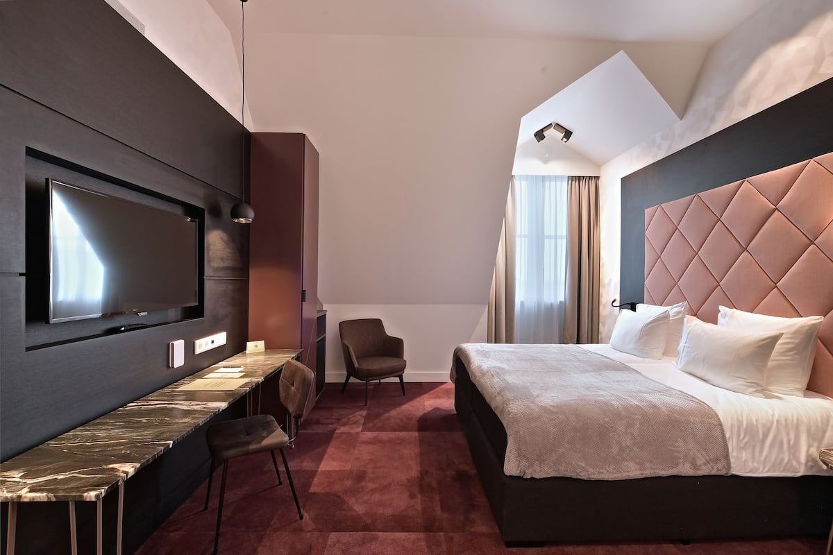 Una habitación de hotel moderna con una cama grande, un televisor de pantalla plana montado en la pared, un escritorio con una silla y una zona de estar acogedora.