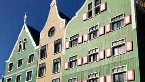 Eine Reihe bunter Gebäude mit unterschiedlichen Baustilen, darunter ein grünes Gebäude mit zahlreichen Fenstern und ein beiges Gebäude mit einem spitz zulaufenden Dach.