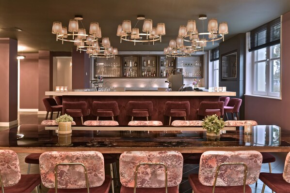 A bar area with a marble countertop, multiple bar stools, and a large chandelier.