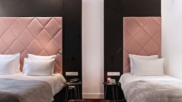 Habitación de hotel con dos camas, cada una con cabecero capitonado, ropa blanca y una mesita de noche con lámpara.