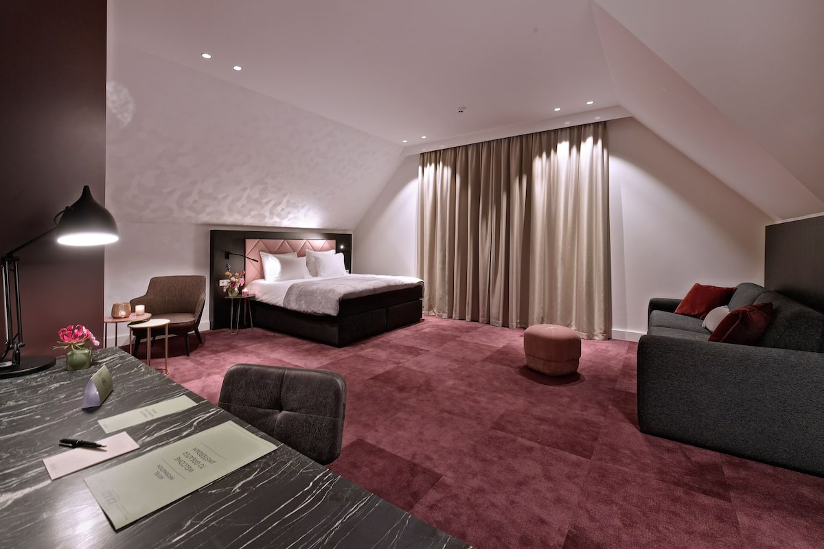 Una habitación de hotel moderna con una cama grande, un escritorio con lámpara, un sofá y una pequeña mesa con un florero.