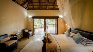 A bedroom with a bed, a chair, a small table, and a window with a view of the outdoors. - The Island River Lodge (Hoedspruit)