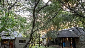 A secluded lodge with a thatched-roof structure, a stone building, and a wooden deck. - The Island River Lodge (Hoedspruit)