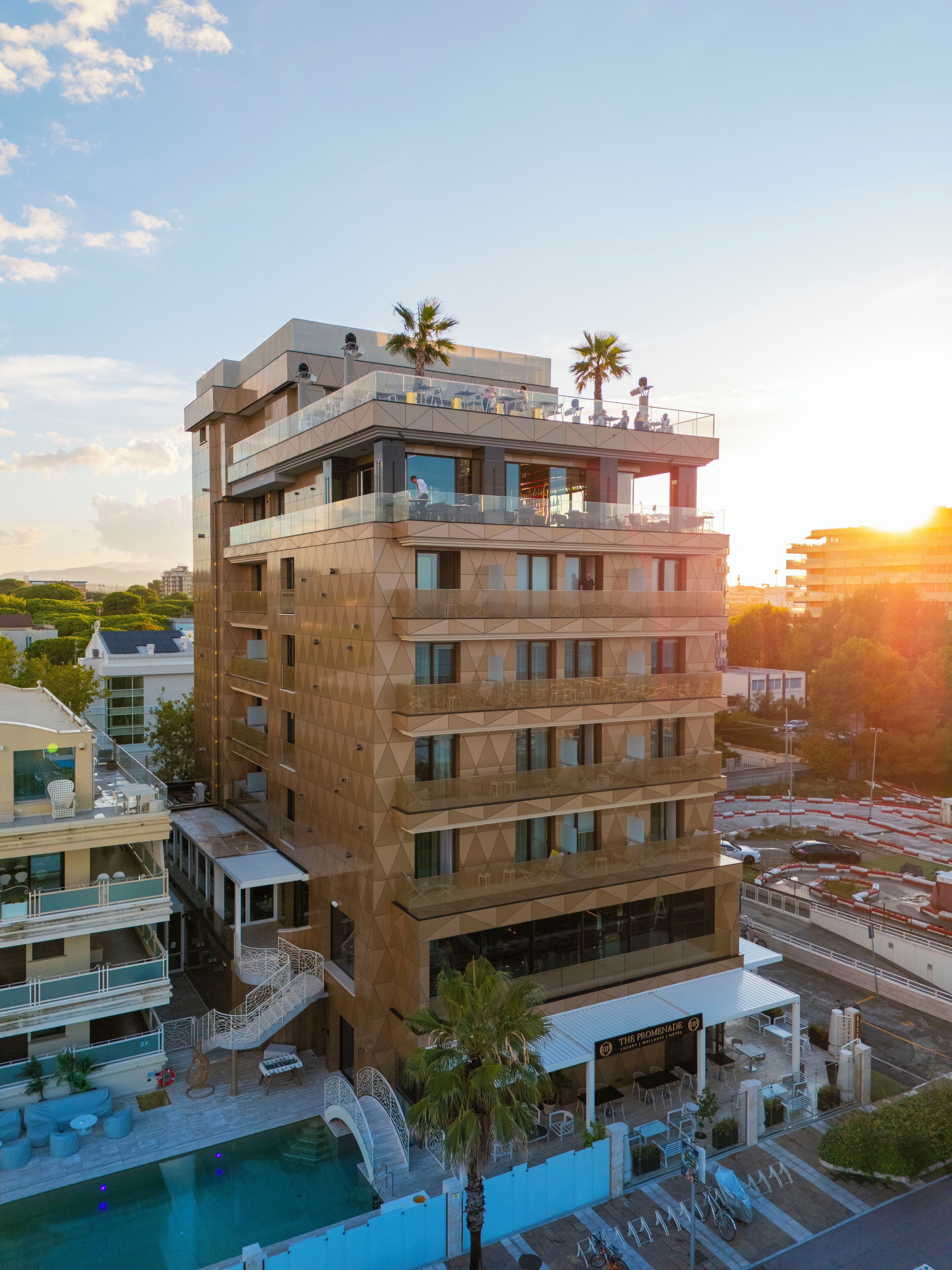 Un hotel de varios pisos con piscina, zona de estar al aire libre y palmeras.