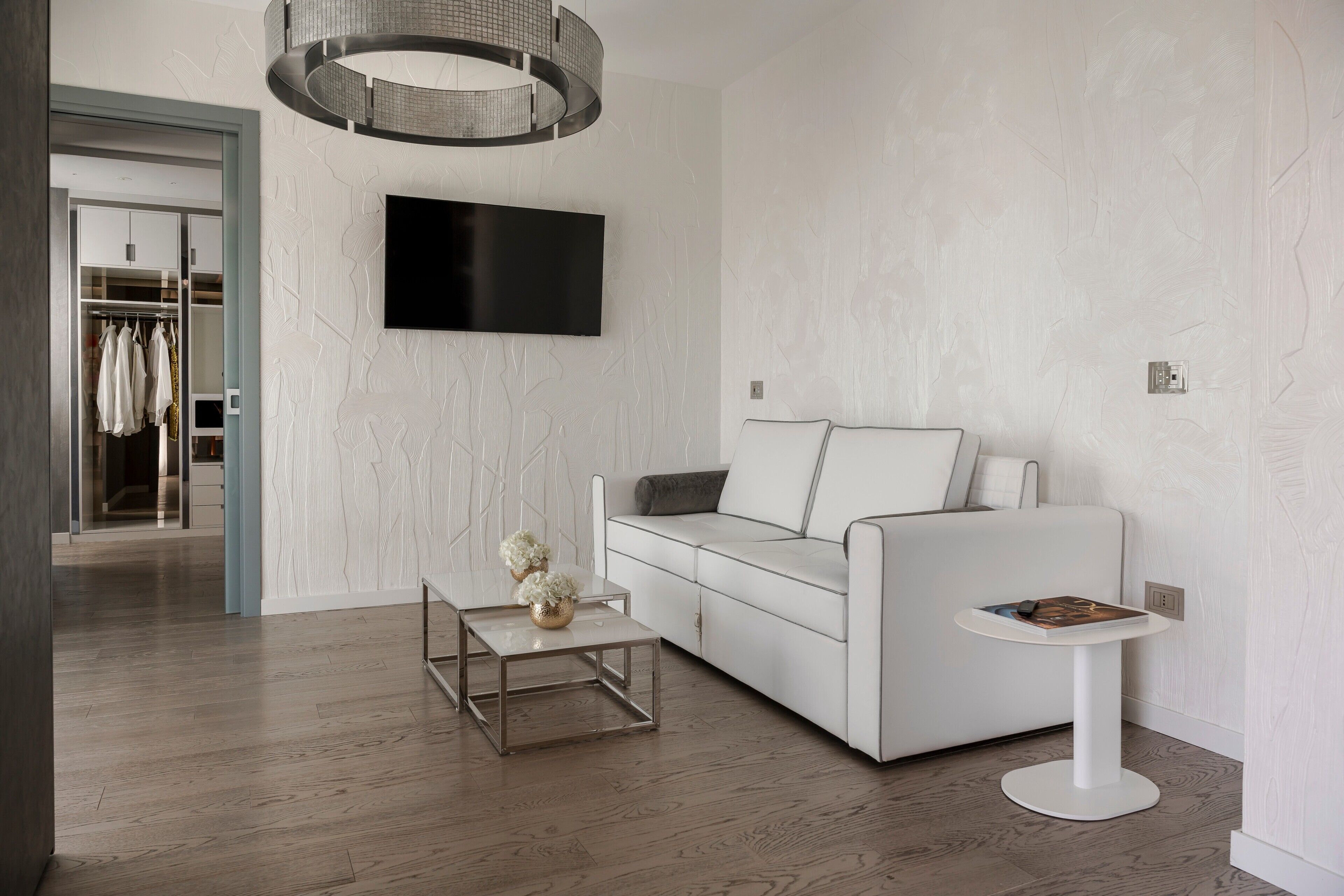 Un salón moderno con un sofá blanco, una mesa de centro y una mesita auxiliar. Un televisor de pantalla plana está montado en la pared sobre el sofá.