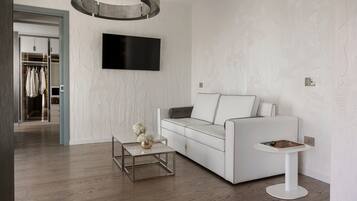 Un salón moderno con un sofá blanco, una mesa de centro y una mesita auxiliar. Un televisor de pantalla plana está montado en la pared sobre el sofá.
