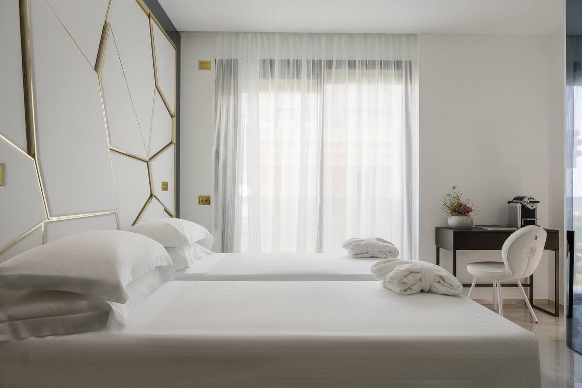 A modern hotel room with two beds, a desk, and a chair.