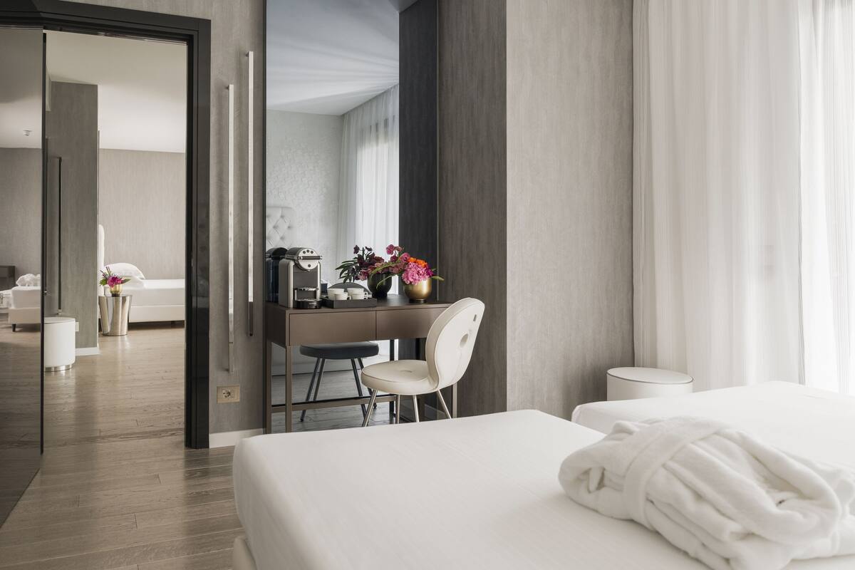 A modern hotel room with a bed, a desk with a chair, and a bathroom visible through an open door.