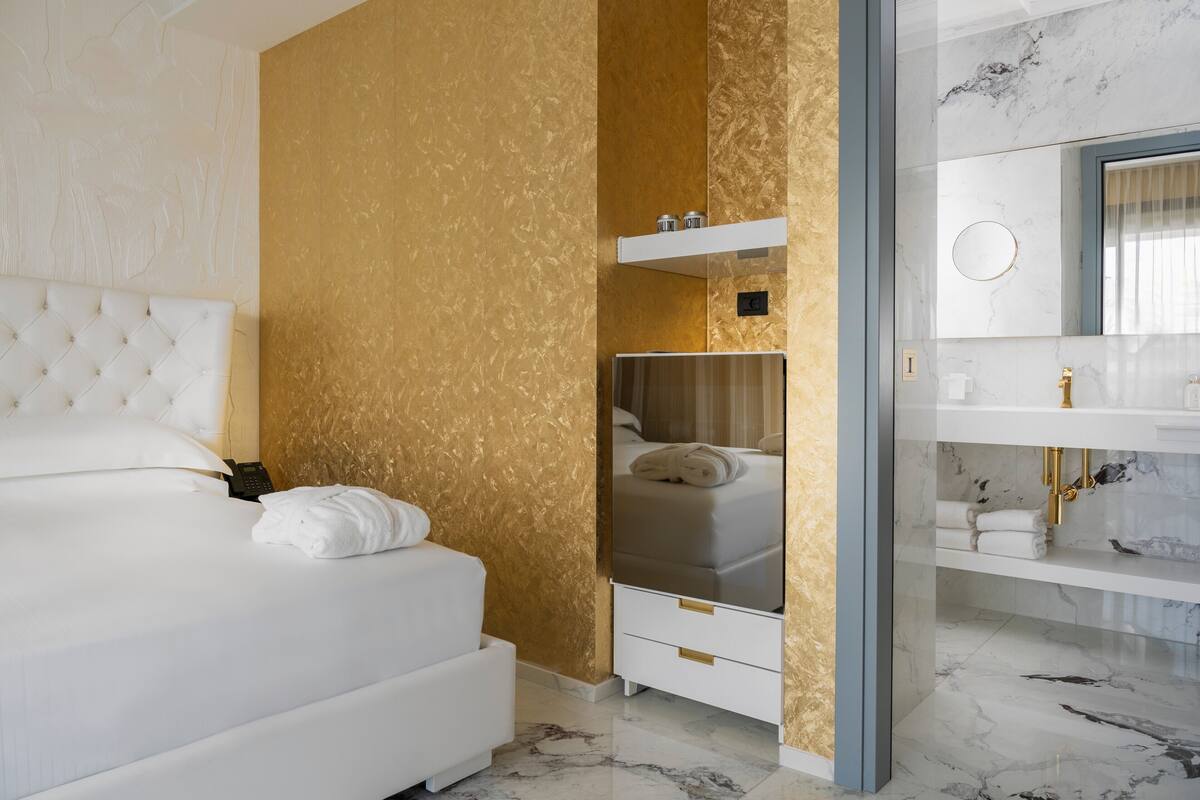 A modern hotel room with a large bed, a vanity with a mirror, and a gold textured wall.