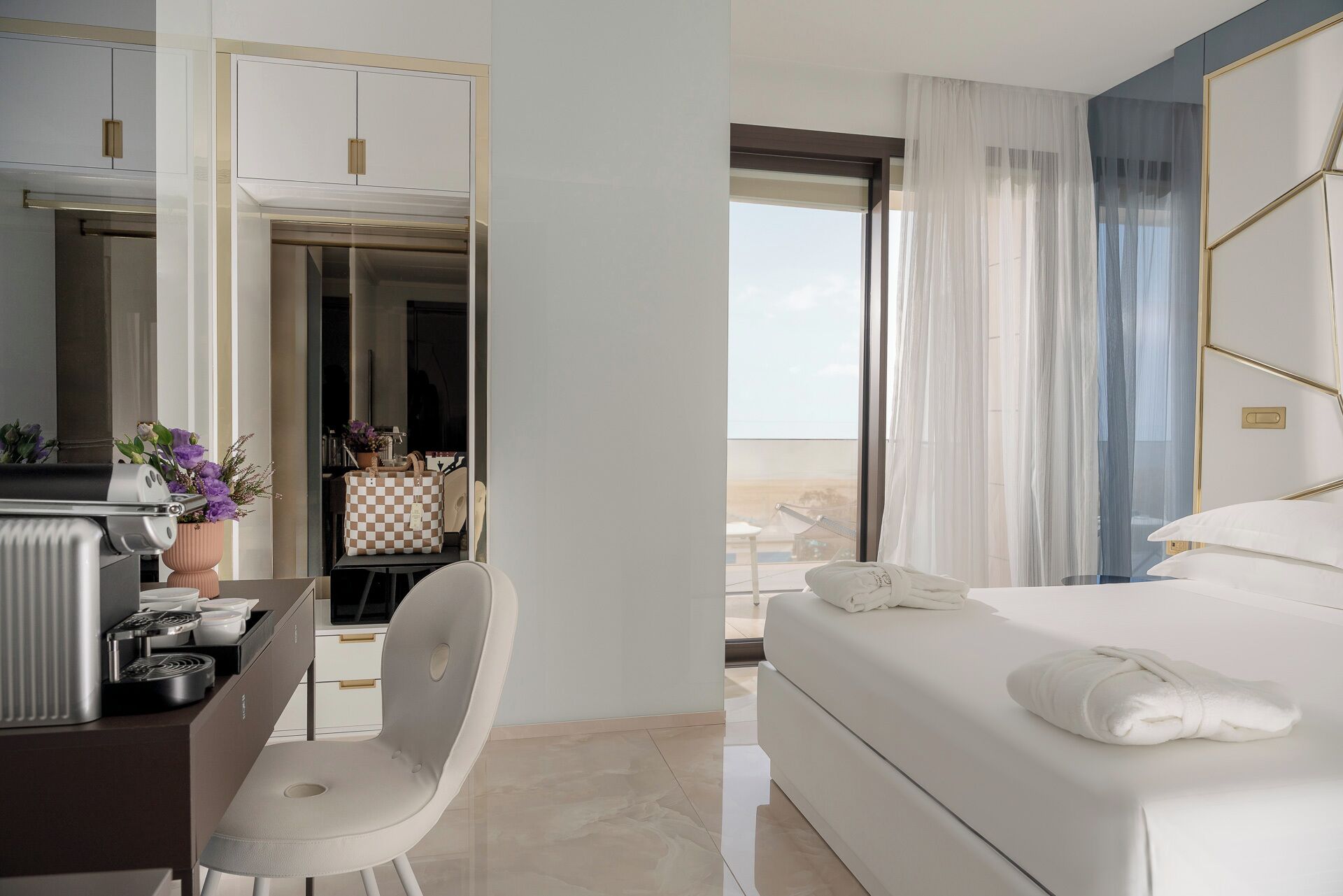 A modern hotel room with a bed, a desk with a chair, a view of the outdoors, and a bathroom with a shower.