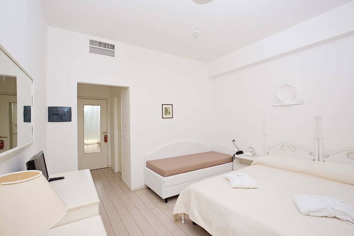 A hotel room with a bed, bedside table, lamp, and a door leading to another room.
