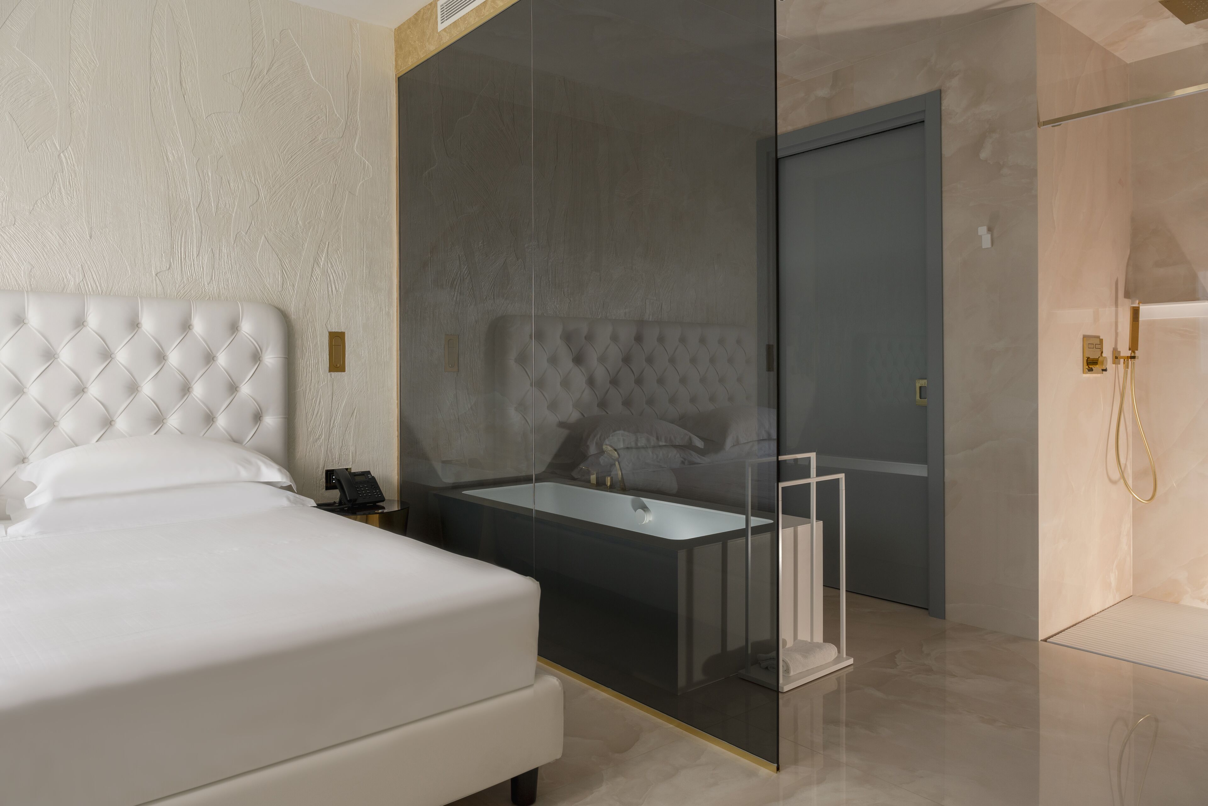 A modern bedroom with a large bed, a glass-enclosed bathroom, and a walk-in closet.